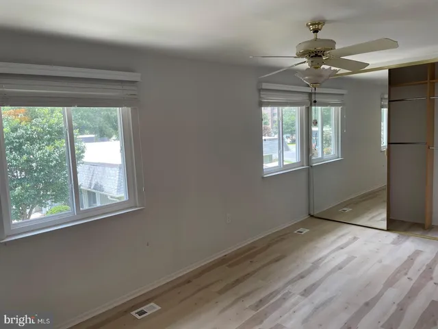 an empty room with wooden floor fan and windows