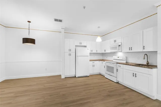 a kitchen with stainless steel appliances granite countertop a sink a stove a refrigerator and white cabinets with wooden floor