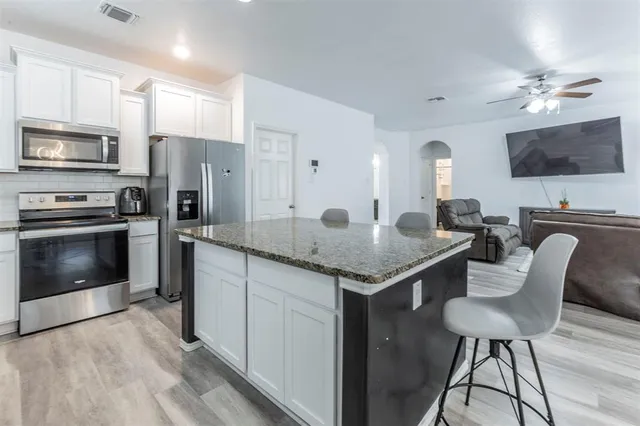 a kitchen with stainless steel appliances a stove a sink dishwasher a refrigerator with a dining table and chairs