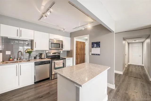 a kitchen with stainless steel appliances granite countertop a refrigerator a stove top oven a sink dishwasher and white cabinets with wooden floor