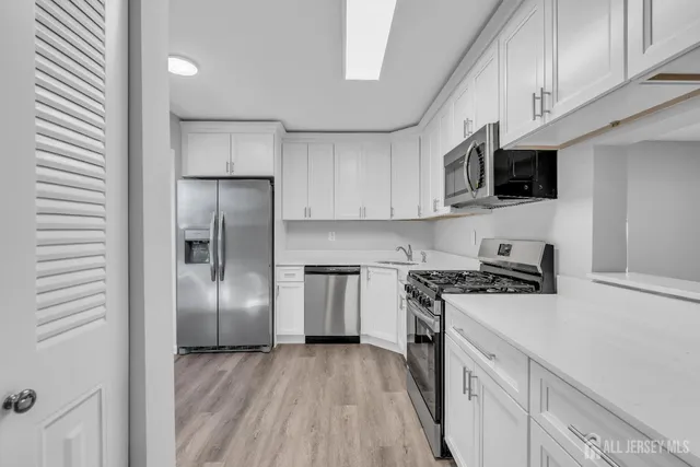 a kitchen with stainless steel appliances granite countertop a refrigerator a stove top oven a sink and cabinets with wooden floor