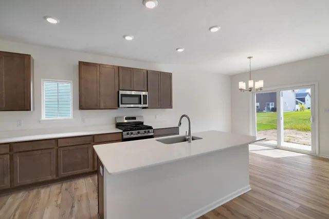 a kitchen with stainless steel appliances a sink a stove a microwave a sink a refrigerator dining table and chairs