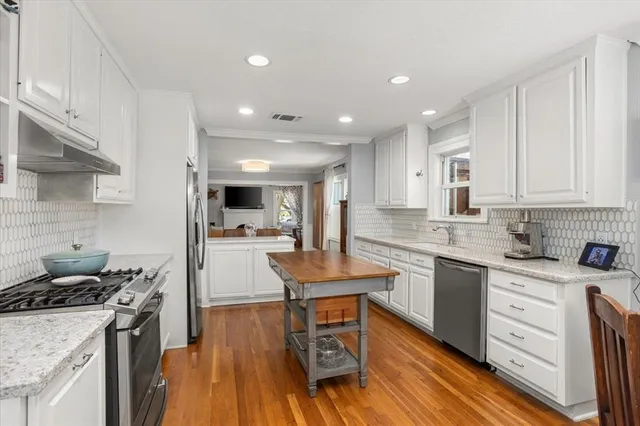 a kitchen with stainless steel appliances granite countertop wooden floor sink stove and white cabinets