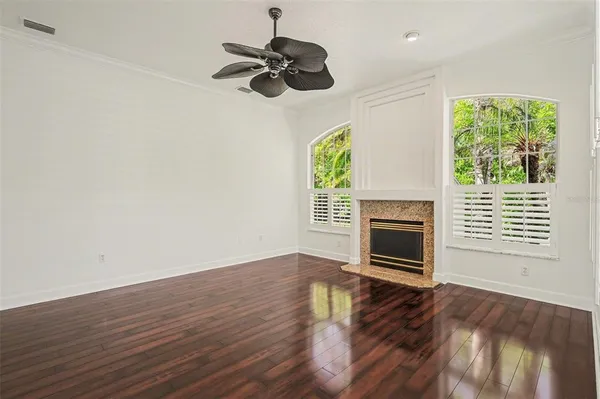 an empty room with windows a fireplace a ceiling fan and wooden floor