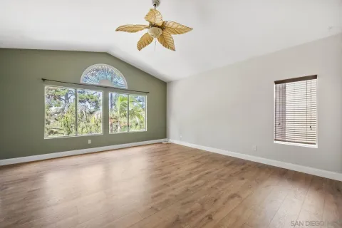 an empty room with wooden floor fan and windows