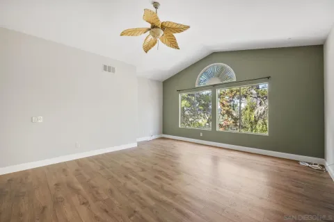 an empty room with wooden floor fan and windows