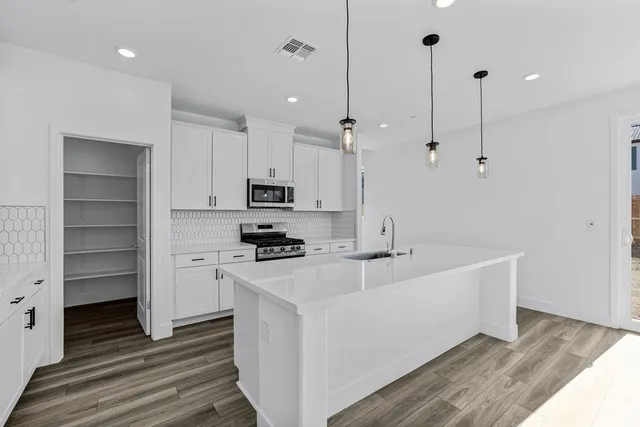 a large white kitchen with kitchen island a stove a sink a refrigerator and white cabinets with wooden floor