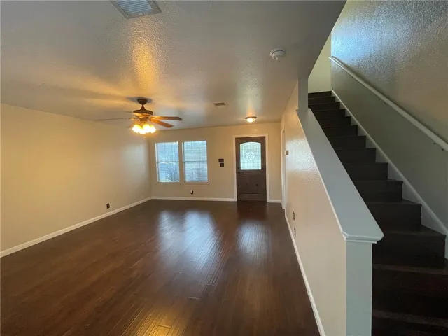 a view of an empty room with wooden floor and fan