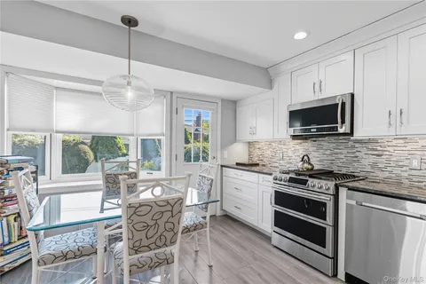 a open kitchen with stainless steel appliances granite countertop a stove top oven a sink dishwasher a dining table and chairs with wooden floor