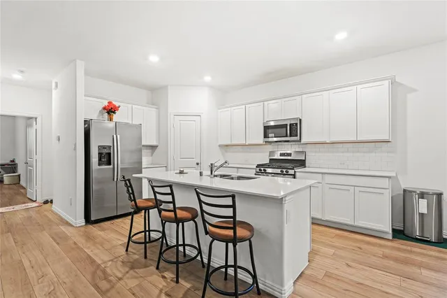a kitchen with stainless steel appliances kitchen island granite countertop a refrigerator a stove top oven a sink dishwasher and white cabinets with wooden floor