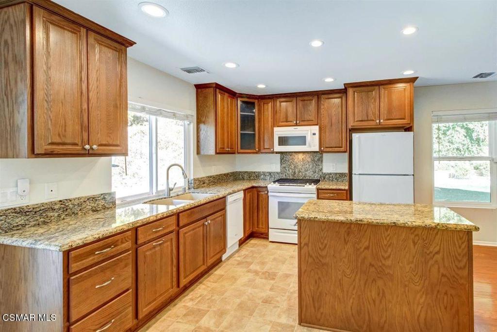 a kitchen with kitchen island granite countertop wooden cabinets a sink a stove a refrigerator and island