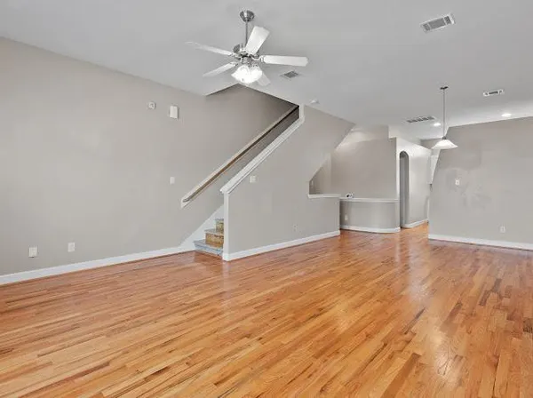 a view of an empty room with wooden floor and a ceiling fan