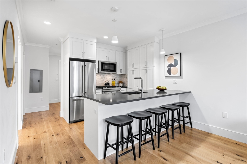 30 Polk Street, Unit 208 Boston, MA 02129 - Photo 3 of 30 a kitchen with stainless steel appliances a dining table chairs refrigerator and microwave