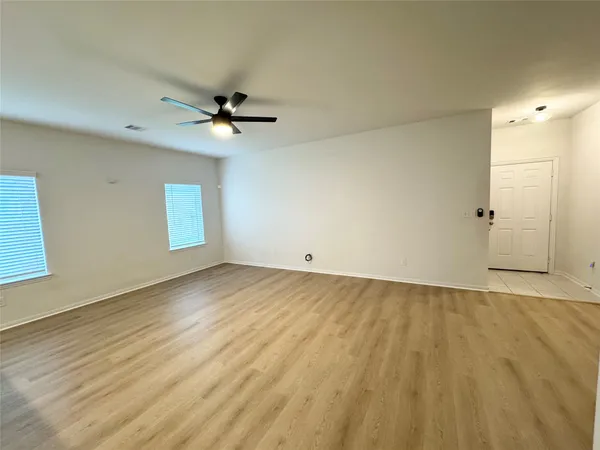 a view of an empty room with wooden floor and a kitchen