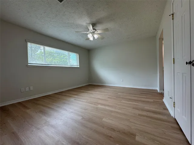 an empty room with wooden floor chandelier fan and windows