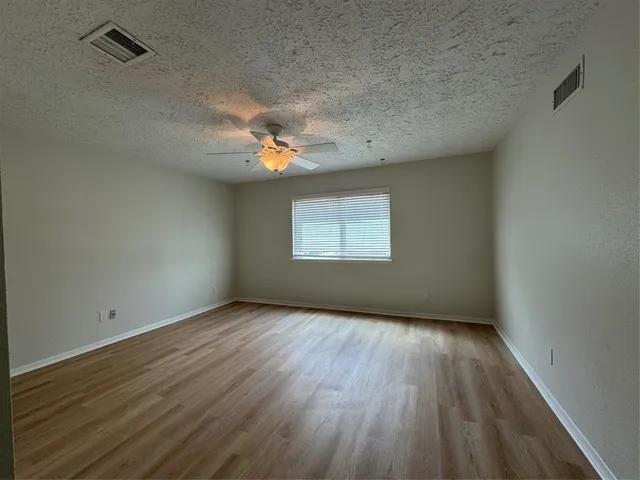 an empty room with wooden floor chandelier fan and windows