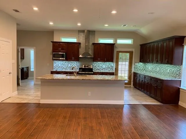 a large kitchen with stainless steel appliances kitchen island a large counter top and wooden floors
