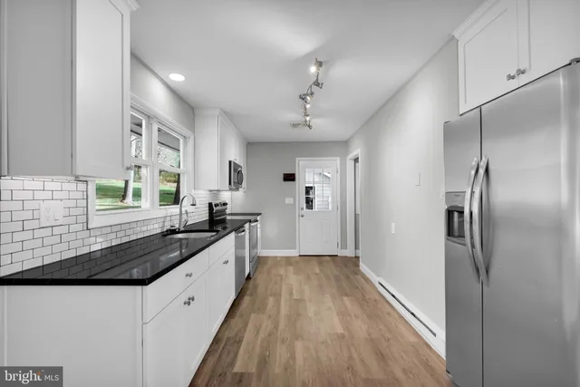 a kitchen with granite countertop a refrigerator a sink a stove and white cabinets