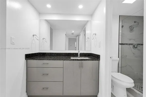 a bathroom with a granite countertop sink a toilet a mirror and shower