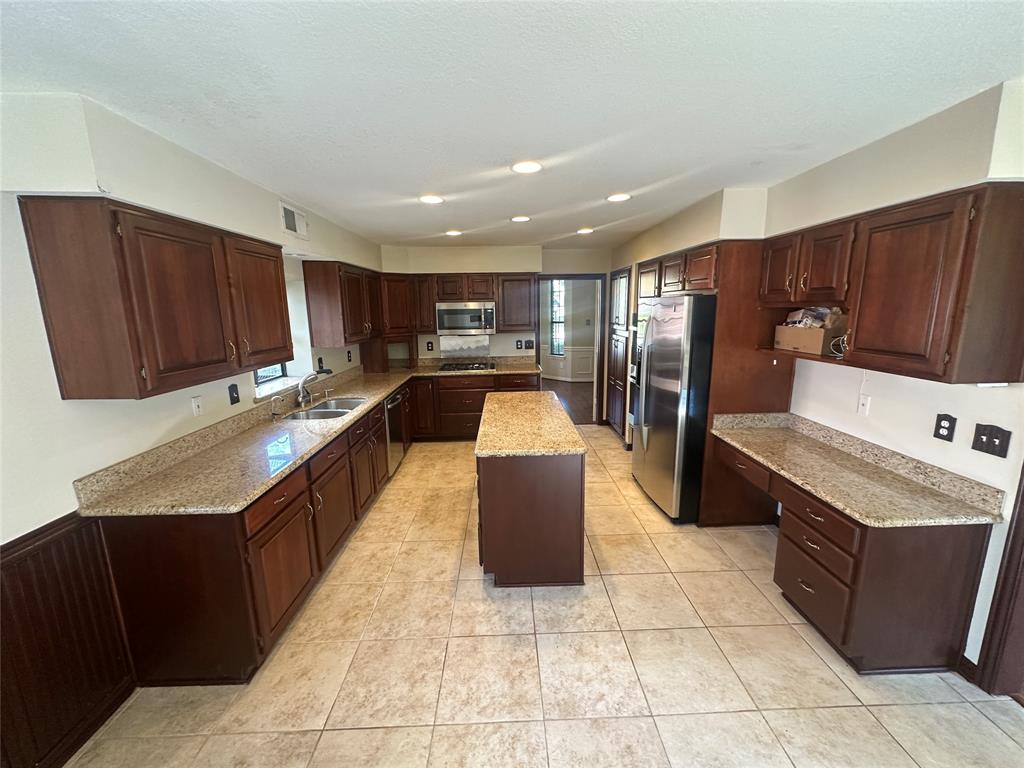 4342 Timberglen Road Dallas, TX 75287 - Photo 12 of 27 Kitchen featuring stainless steel appliances, a kitchen island, dark wood finish cabinetry, light stone counters, and recessed lighting