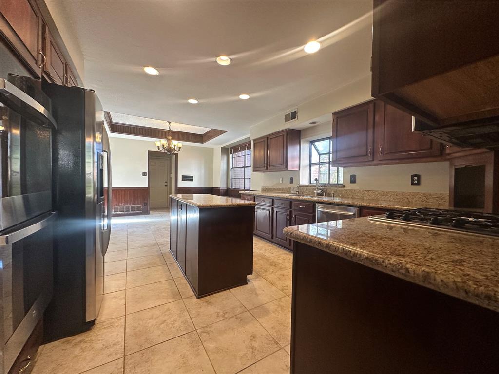 4342 Timberglen Road Dallas, TX 75287 - Photo 14 of 27 Kitchen with a kitchen island, dark wood finish cabinets, dark stone counters, range hood, and a chandelier