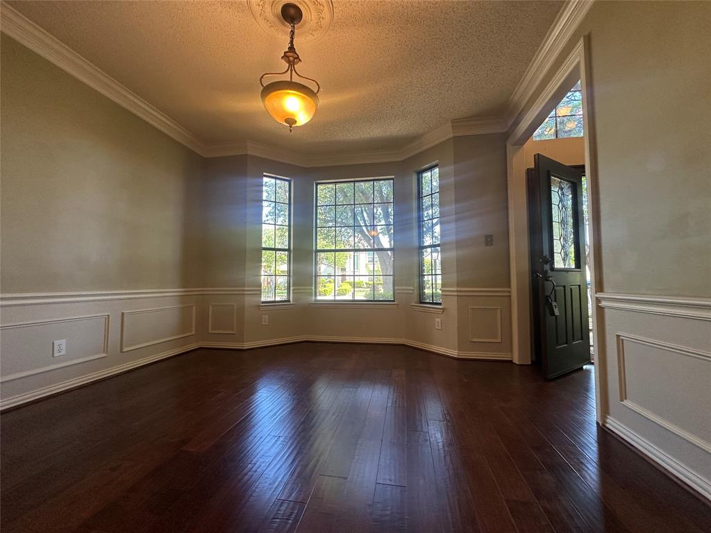 4342 Timberglen Road Dallas, TX 75287 - Photo 15 of 27 Unfurnished room featuring a textured ceiling, a decorative wall, a wainscoted wall, and dark wood-style flooring