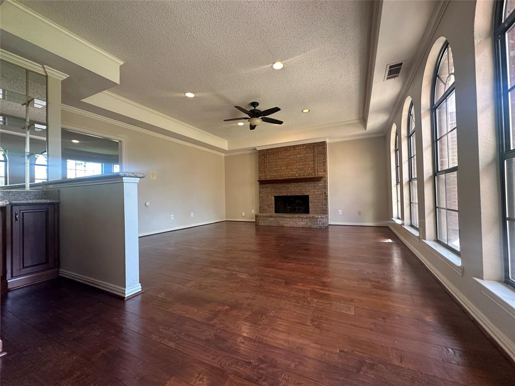 4342 Timberglen Road Dallas, TX 75287 - Photo 2 of 27 Unfurnished living room featuring a tray ceiling, dark wood finished floors, a ceiling fan, ornamental molding, and a textured ceiling