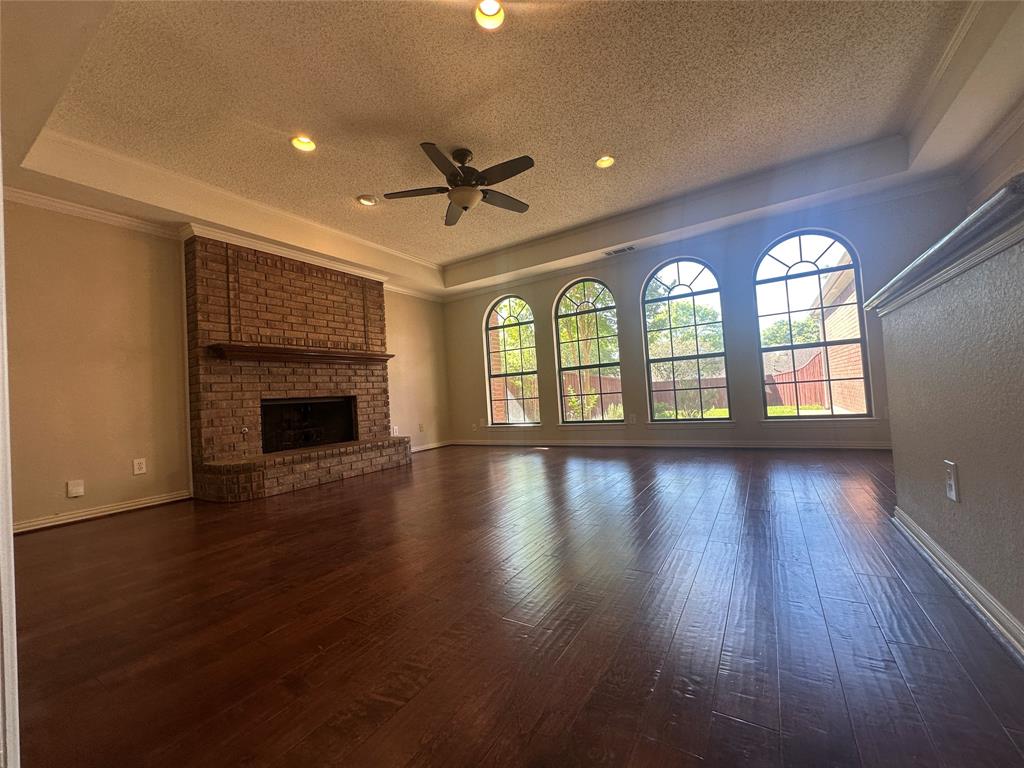 4342 Timberglen Road Dallas, TX 75287 - Photo 4 of 27 Unfurnished living room with a raised ceiling, ceiling fan, dark wood-style floors, ornamental molding, and a textured ceiling
