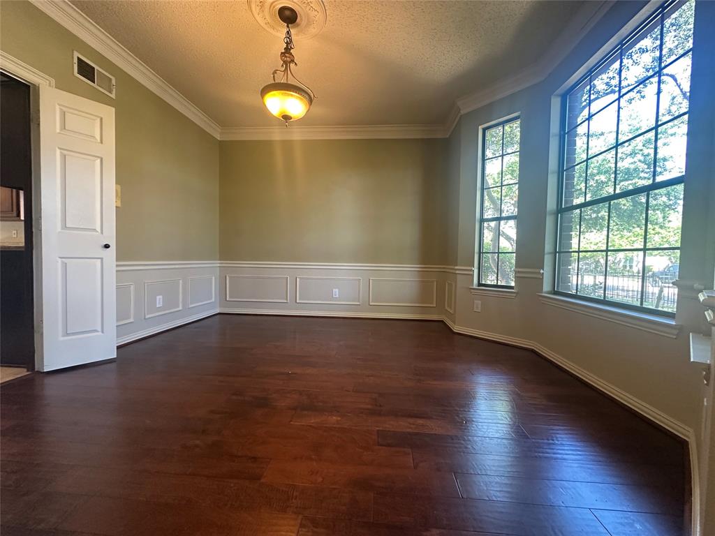 4342 Timberglen Road Dallas, TX 75287 - Photo 5 of 27 Spare room with a textured ceiling, ornamental molding, dark wood-style floors, a wainscoted wall, and a decorative wall