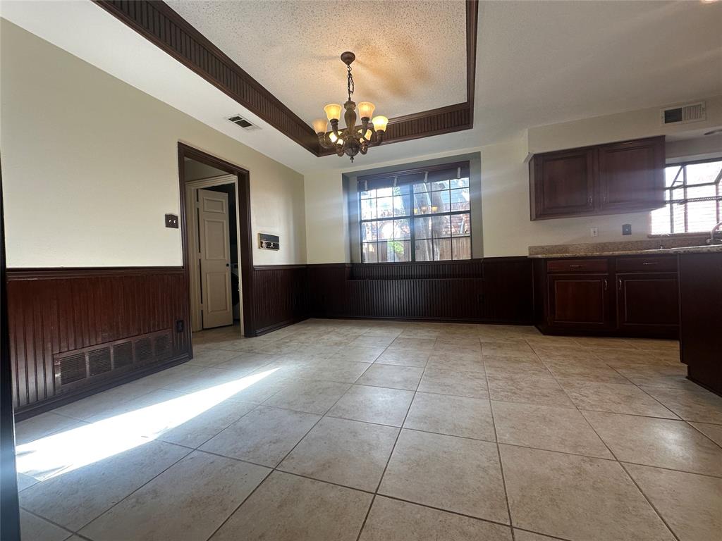 4342 Timberglen Road Dallas, TX 75287 - Photo 10 of 27 Unfurnished dining area featuring a wainscoted wall, hanging lights, a raised ceiling, wood walls, and a textured ceiling