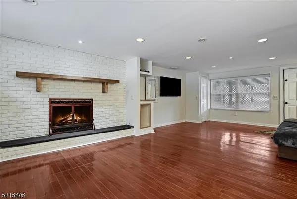 a view of an empty room with wooden floor fireplace and a window