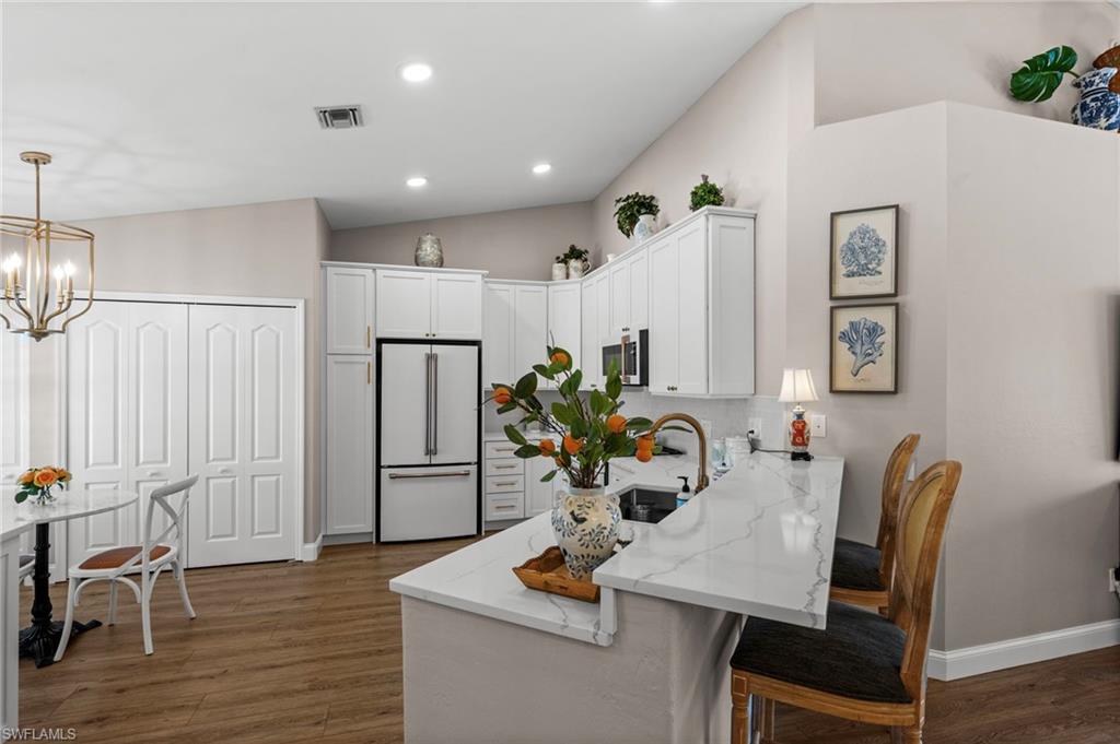 9331 Spring Run Boulevard, Unit 3005 Estero, FL 34135 - Photo 9 of 48 Vaulted ceilings, wood-finish flooring, white cabinetry, integrated stainless steel appliances, and a kitchen island with a waterfall countertop