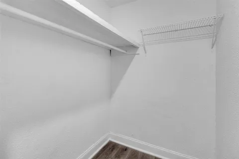 a view of an empty room with wooden floor and a kitchen