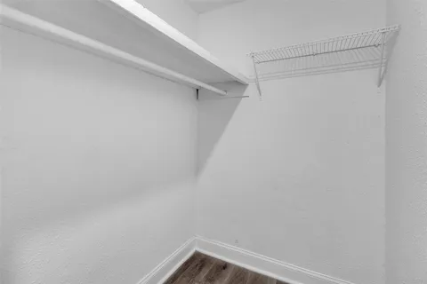 a view of an empty room with wooden floor and a kitchen