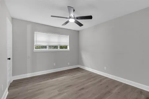 an empty room with wooden floor chandelier fan and windows