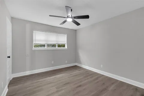 an empty room with wooden floor chandelier fan and windows
