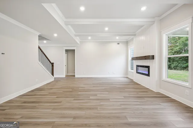 a view of an empty room with wooden floor and a kitchen