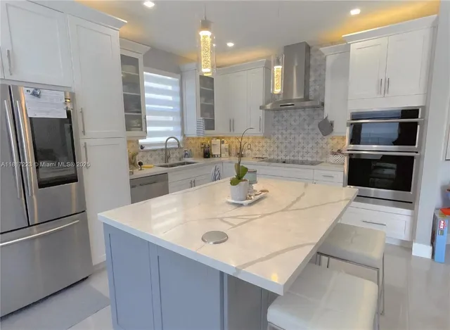 a kitchen with stainless steel appliances kitchen island granite countertop a sink a stove a refrigerator a washer dryer and cabinets