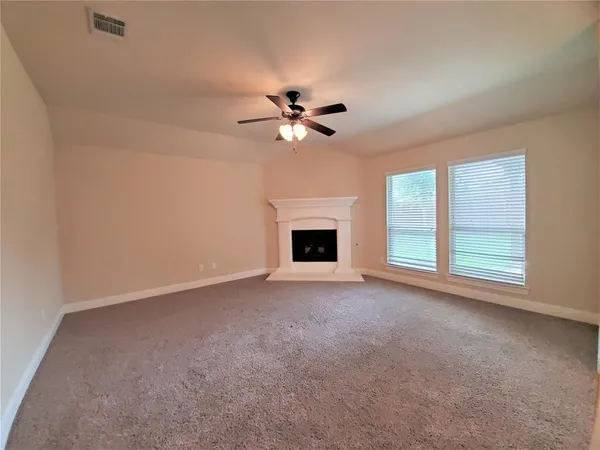 an empty room with windows fireplace and a ceiling fan