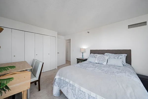 a bedroom with a bed a chair and potted plant on the dresser