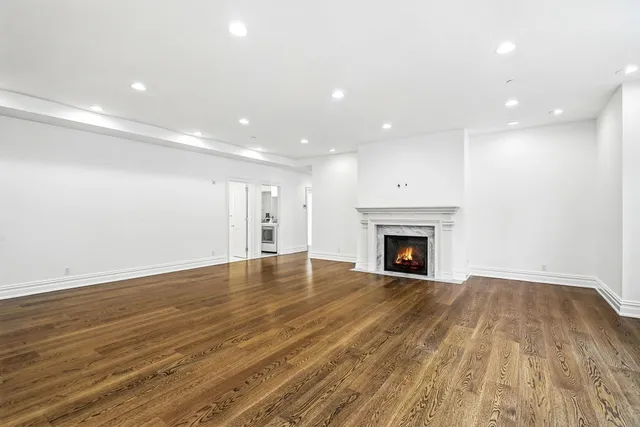 a view of an empty room with wooden floor fireplace and a window