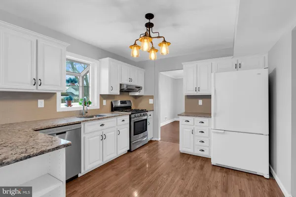 a kitchen with granite countertop a refrigerator a stove a sink and white cabinets with wooden floor