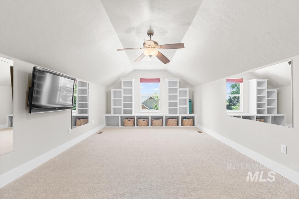 23800 Breyer Road Caldwell, ID 83607 - Photo 32 of 50 Spacious room featuring vaulted ceilings, neutral-toned carpet flooring, a ceiling fan, and built-in shelving with storage nooks flanking two windows
