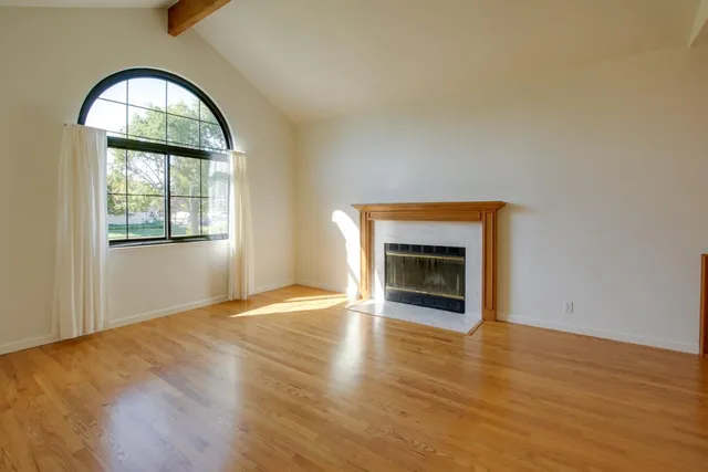 an empty room with wooden floor fireplace and windows