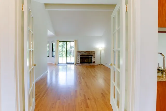 a view of a hallway to an empty room with wooden floor and a window