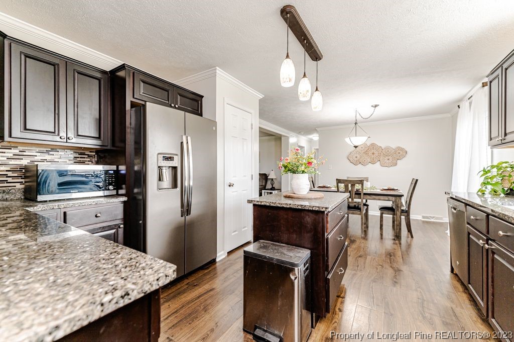 125 Wright Road Vass, NC 28394 - Photo 14 of 48 a kitchen with granite countertop kitchen island stainless steel appliances a stove refrigerator a sink a dining table and chairs with wooden floor