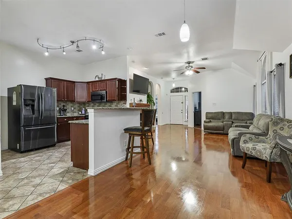 a kitchen with stainless steel appliances kitchen island granite countertop a refrigerator a stove a sink a dining table and chairs with wooden floor