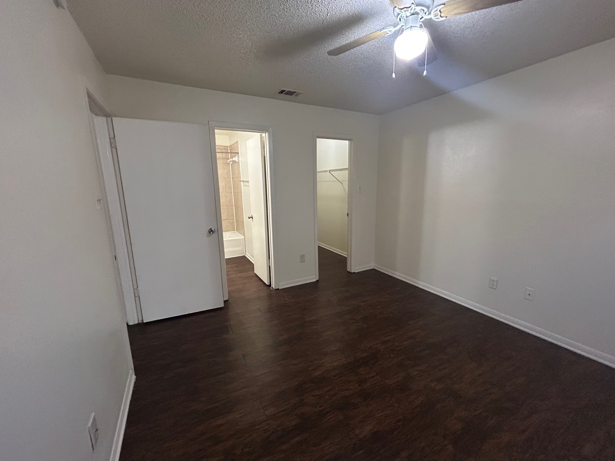 8812 Schick Road, Unit C Austin, TX 78729 - Photo 11 of 12 Unfurnished bedroom featuring dark wood finished floors, a textured ceiling, a ceiling fan, and a walk in closet