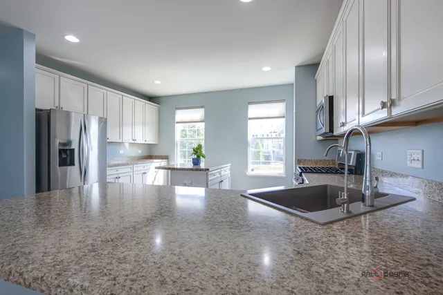 a kitchen with stainless steel appliances granite countertop a refrigerator a sink a stove and white cabinets with wooden floor