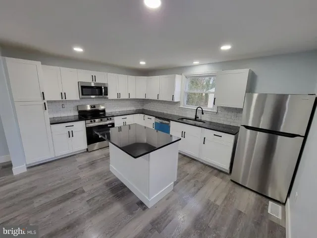 a kitchen with stainless steel appliances a refrigerator a sink a stove a microwave a center island and cabinets